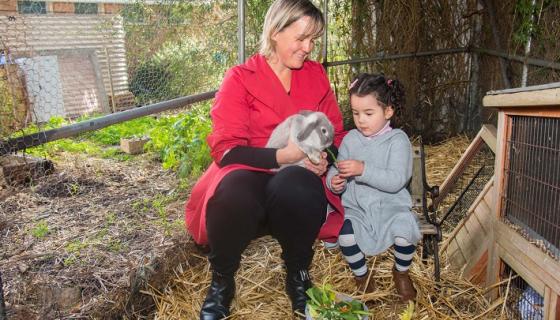 Female educator with preschool girl and rabbit on bench