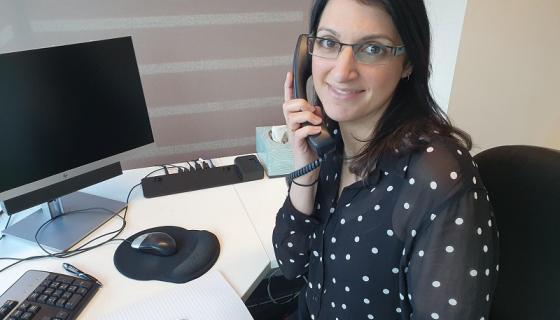 Professional-looking woman at desk in front of computer holding phone and smiling slightly 